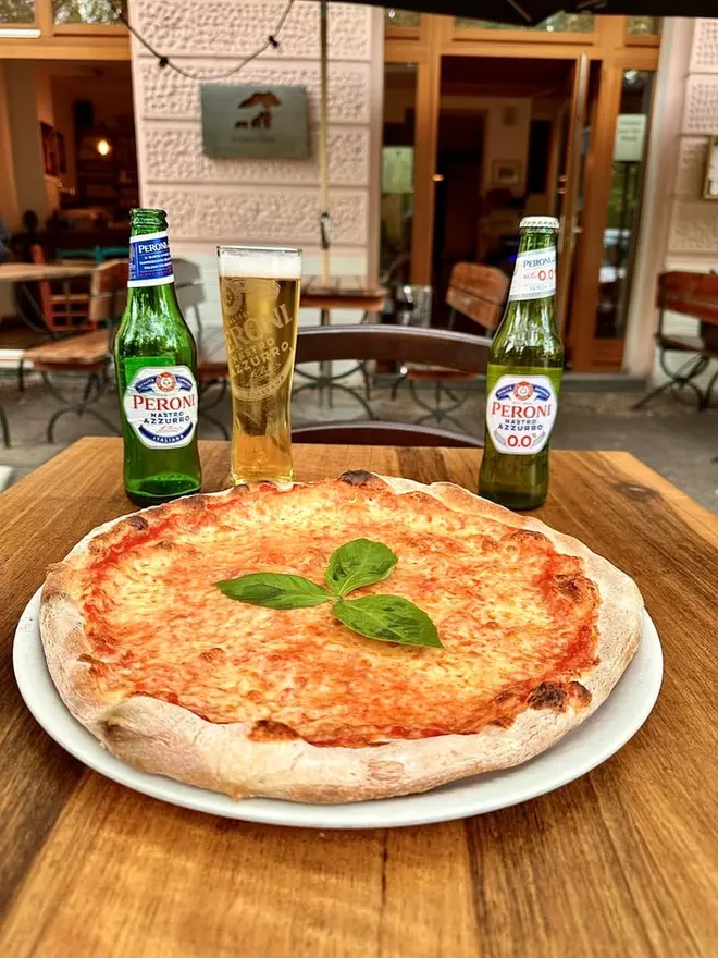 Pizza Margherita auf einem Holztisch vor dem Eingang von La lupa e l’orso